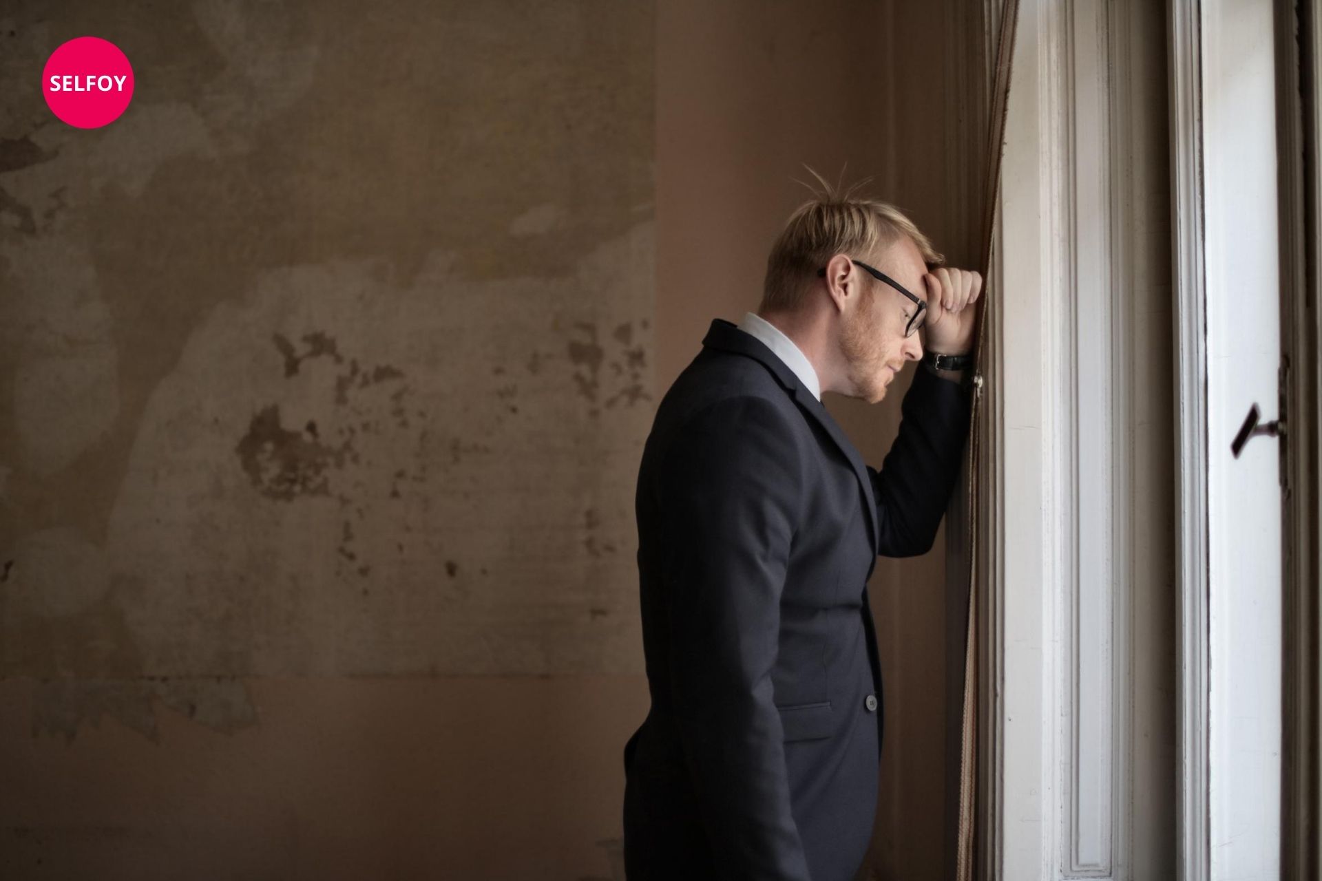 Man in black suit watching through window and thinking about does autodidact work with self care