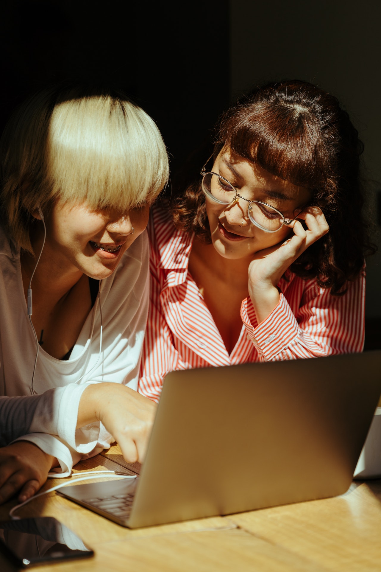 two girl are smiling & watching at laptop screen making social media post