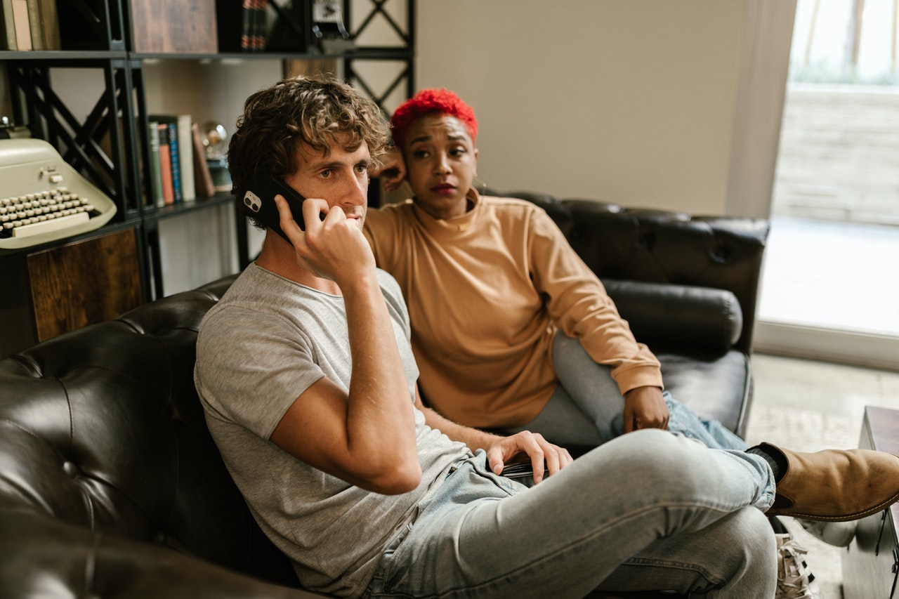 one men and woman sitting on couch and man having phone call