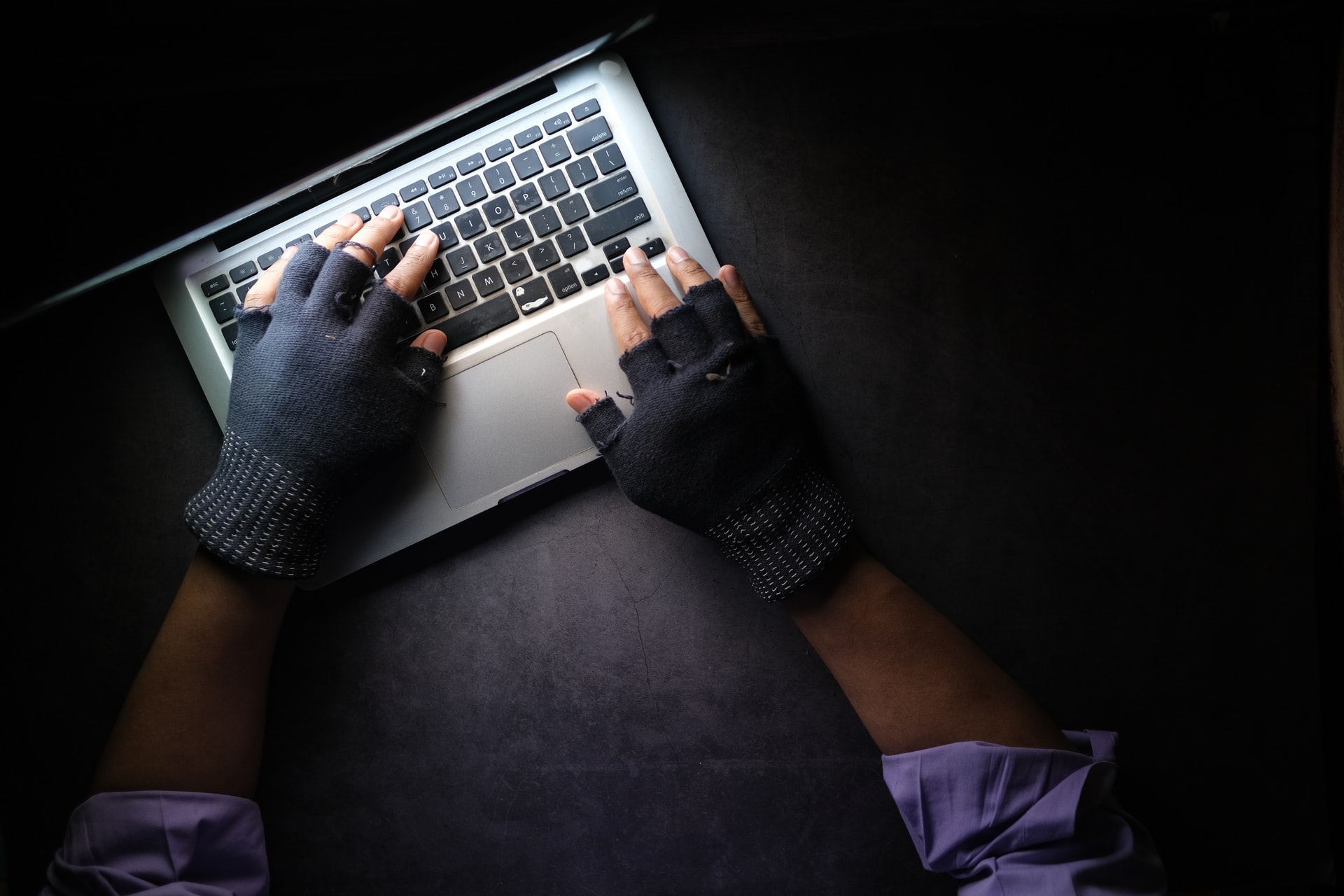 Person wearing black colored gloves typing on a laptop keyboard